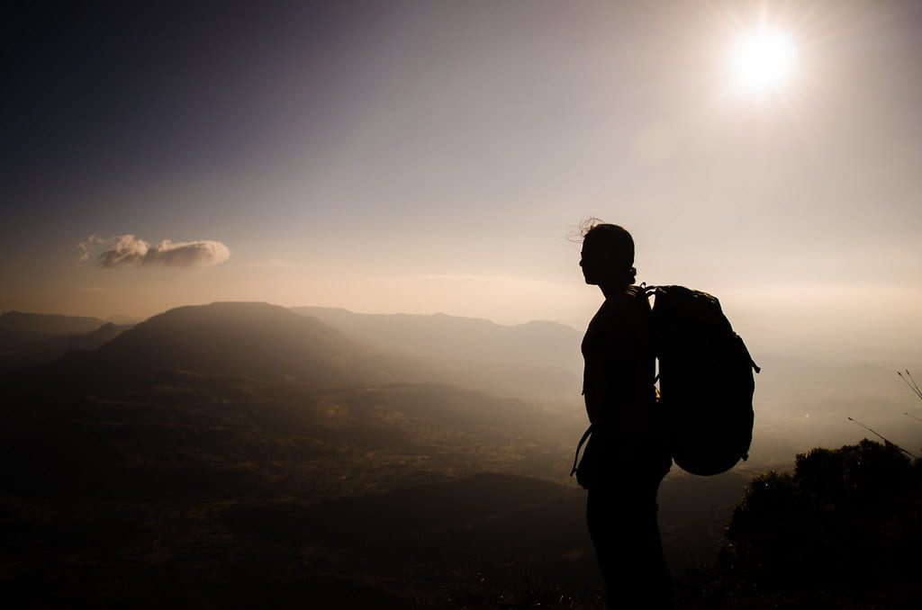 A silhouette of a hiker wearing a backpack overlooking a hazy landscape.